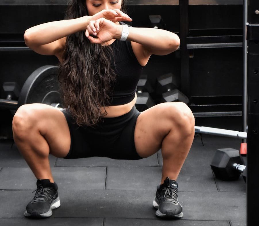 Focused woman squatting in a gym setting surrounded by kettlebells, showcasing determination and fitness.