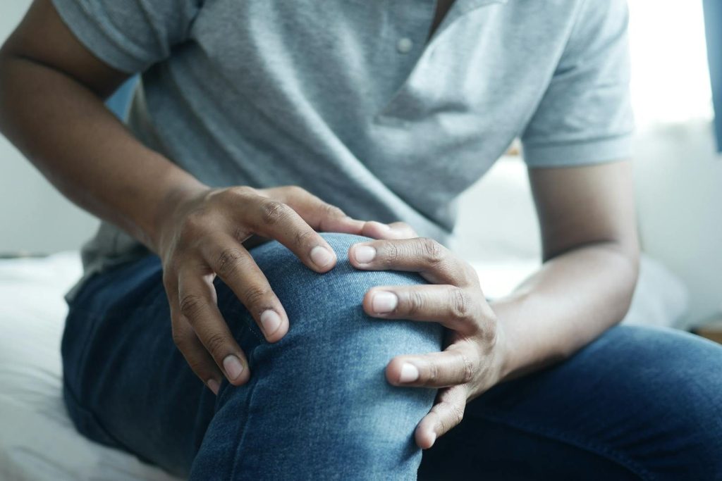 Close-up of a man holding his knee, capturing a moment of discomfort in a casual indoor setting.