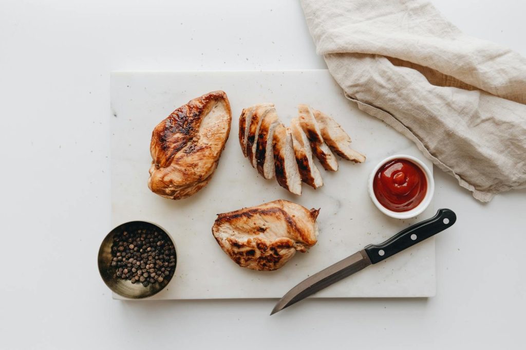 Delicious grilled chicken breast slices on a cutting board with peppercorns and ketchup.