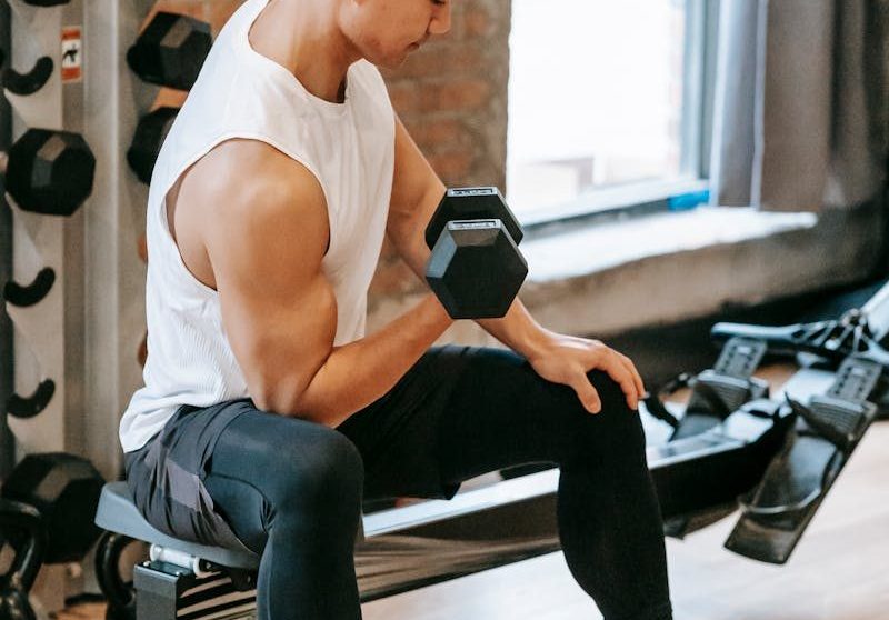 Focused Asian man lifting a dumbbell at an indoor gym, showcasing strength and fitness.