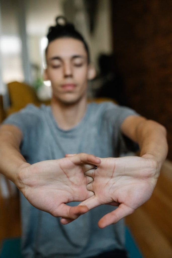 Teenage boy focusing on hand stretches during a workout session indoors.