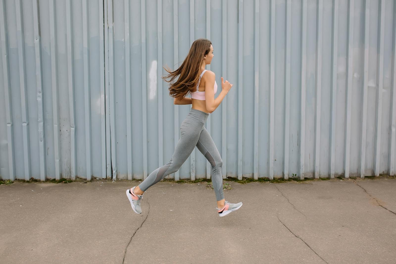 Fit woman running outdoors in activewear with sports bra and leggings. Motion captured at day time.