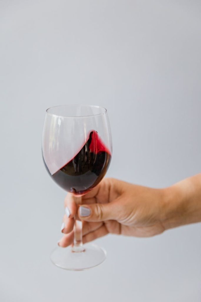 A close-up of a hand holding a red wine glass against a neutral background.