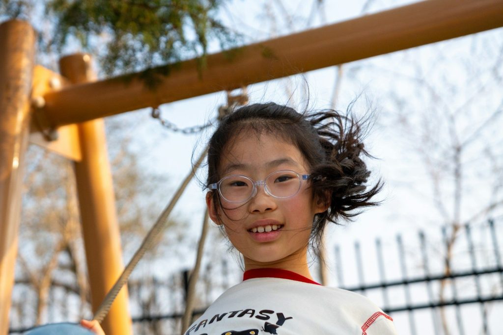 A young girl with glasses smiles outdoors